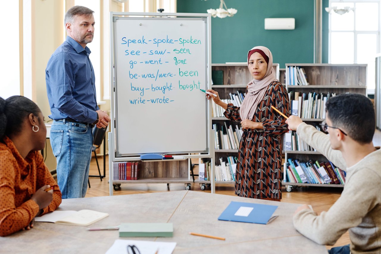 TESOL trainee teacher instructing a diverse group of adult language learners in a classroom setting, demonstrating interactive teaching techniques